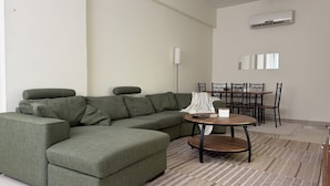 A modern living room with a sectional sofa, a round coffee table, and a dining area with chairs and a table. - The Hive - Cozy 2BR Apartment with Rooftop Pool, Al Khuwair Muscat (Muscat)