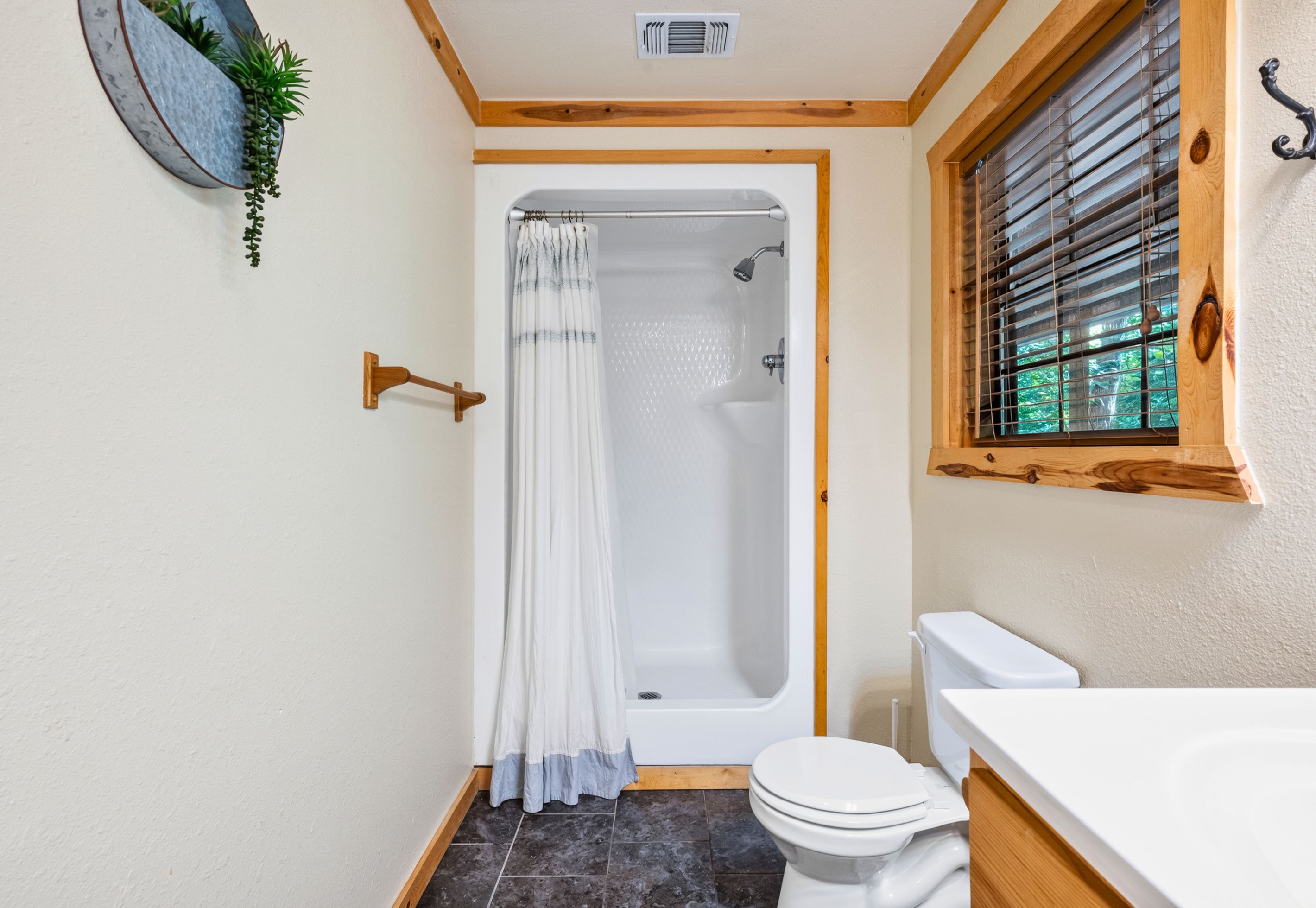 A bathroom with a shower, toilet, and a window with blinds.