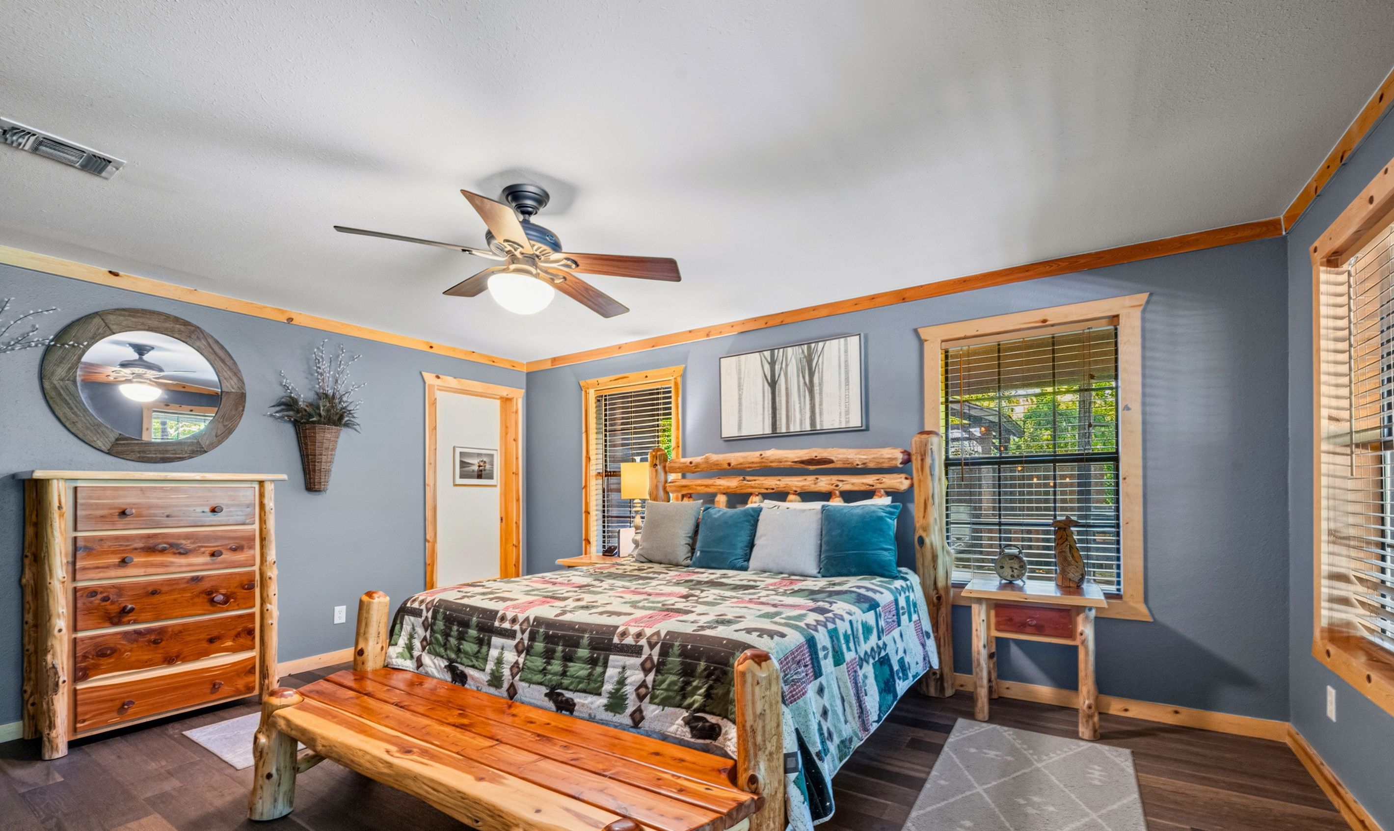 Une chambre à coucher avec un lit en bois, un ventilateur de plafond, une commode et une fenêtre avec des stores.