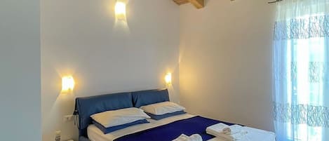 A bedroom with a wooden ceiling, a bed with blue bedding, bedside lamps, and a window with curtains.