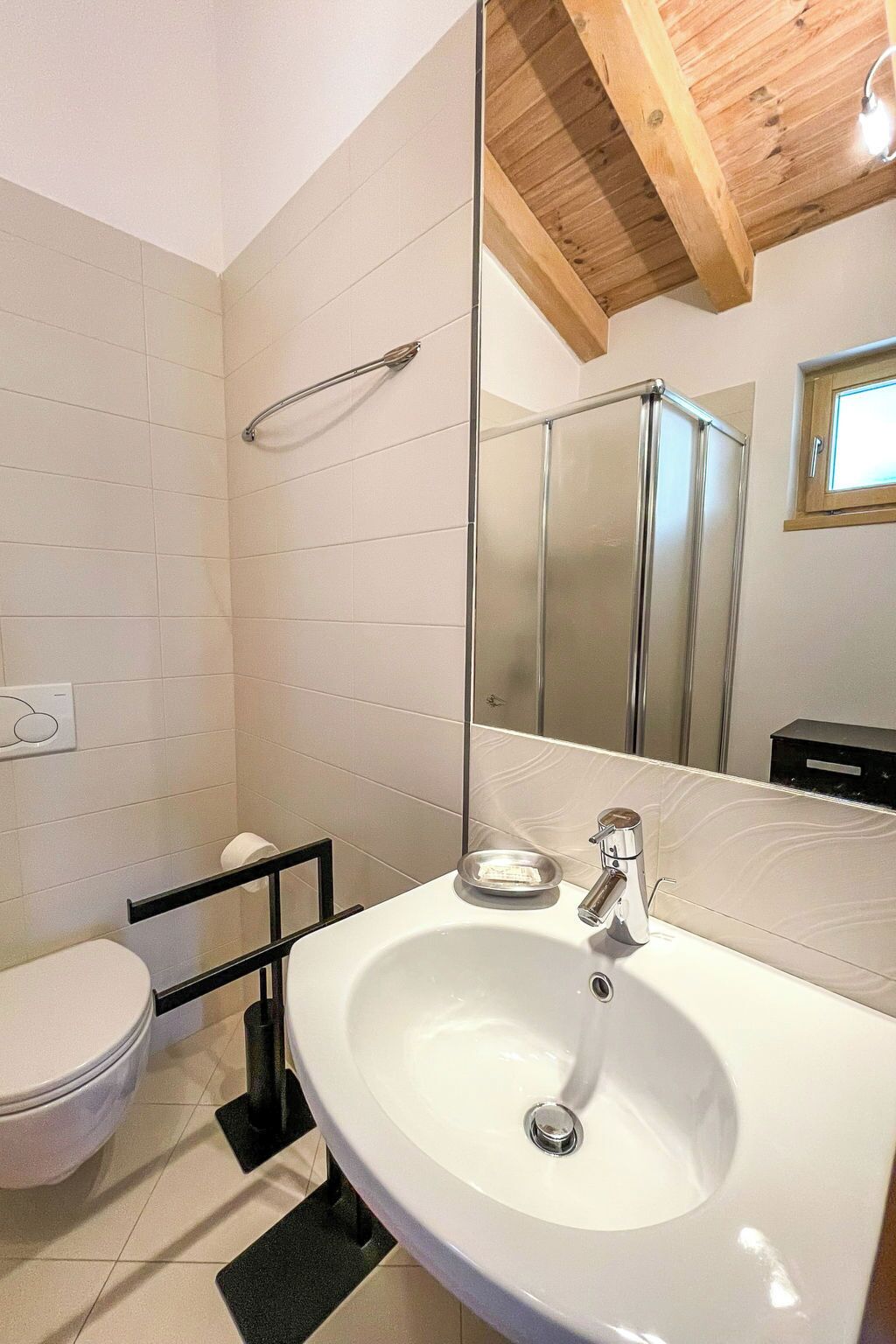 Une salle de bain avec un lavabo blanc, des toilettes, une douche et un miroir qui reflète l’espace de la douche.