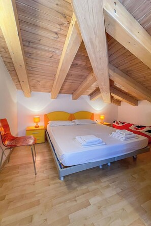 A bedroom with a wooden ceiling, a bed with white linens, a red chair, and bedside lamps. - Vacation home Volme by Interhome (Pula/Banjole)