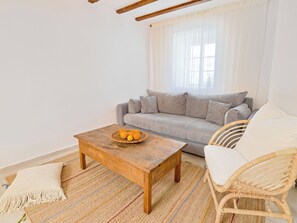 A living room with a sofa, a wooden coffee table with fruit, a woven rug, and a wicker chair. - Vacation home Marina by Interhome (Marina)