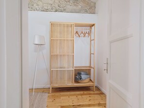 Ein Holzkleiderschrank mit Kleiderstange, ein Korb voller gefalteter Kleidung und eine Stehlampe.