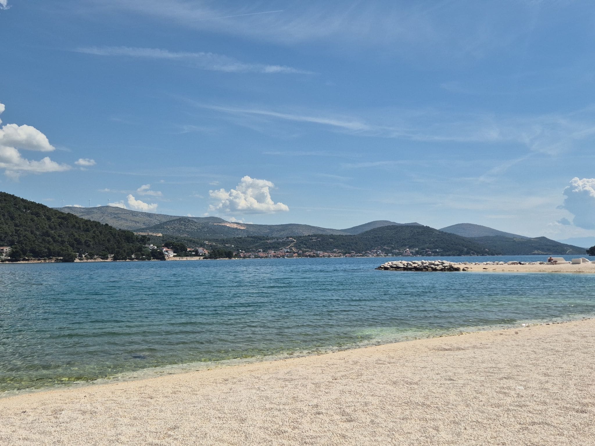 Paisaje costero con cielo despejado, mar tranquilo y una playa de arena.