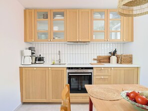 A modern kitchen with wooden cabinets, a built-in oven, and a dining area with a table and chairs. - Vacation home Marina by Interhome (Marina)