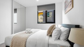 A modern hotel room with a bed, a window with a city view, and a painting on the wall. - Your Melbourne Getaway Base in Carlton (Carlton)