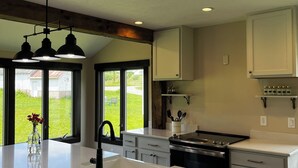 A kitchen with a large island, a built-in oven, and a window with a view of a green lawn. - Charming Farmhouse on a Cherry Orchard just a few minutes from the beach. (Suttons Bay)