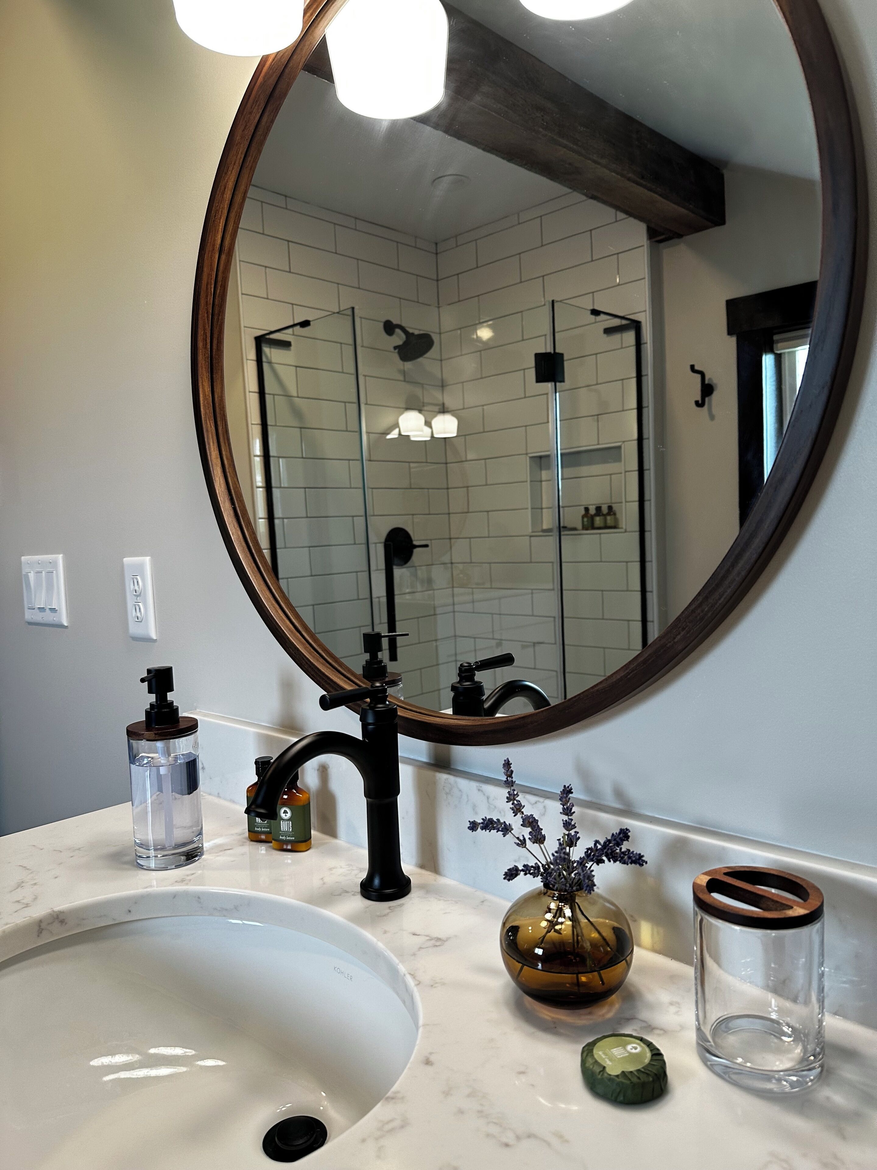 A bathroom with a white sink, a round mirror, and a glass shower enclosure.