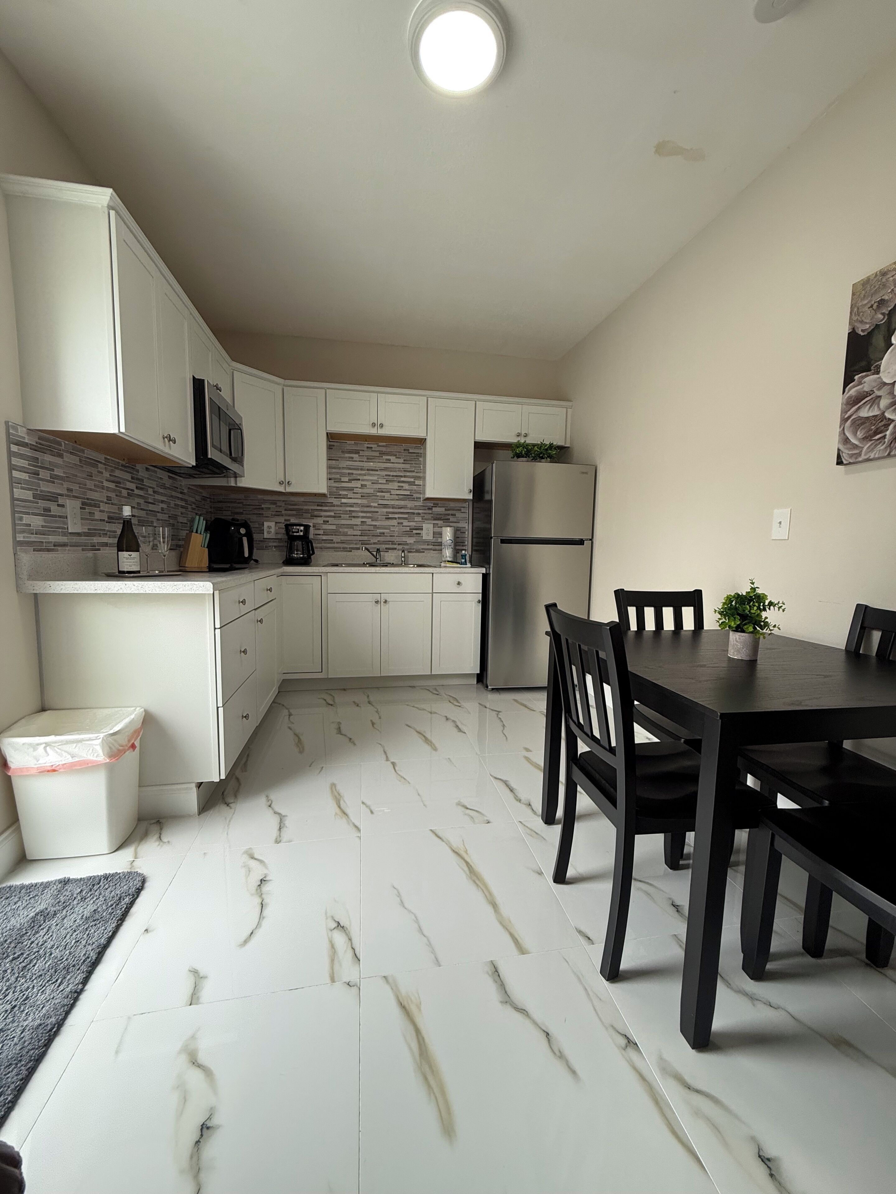 A compact kitchen with white cabinets, a stainless steel refrigerator, and a dining area with a table and chairs.