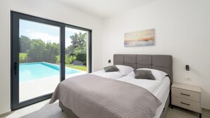 A bedroom with a bed, a nightstand, a painting, and a sliding glass door leading to a pool. - Villa Yamila (Istria - Žminj) (Žminj)