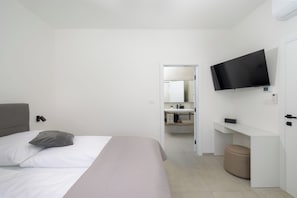 Ein modernes Hotelzimmer mit Bett, Fernseher, Schreibtisch und einem durchgegangenen Tür sichtbaren Badezimmer.