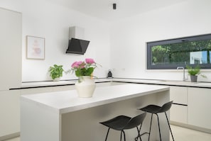Eine moderne Küche mit einer zentralen Kochinsel, Barhocker, einem Fenster und einem an der Wand montierten Flachbildfernseher.