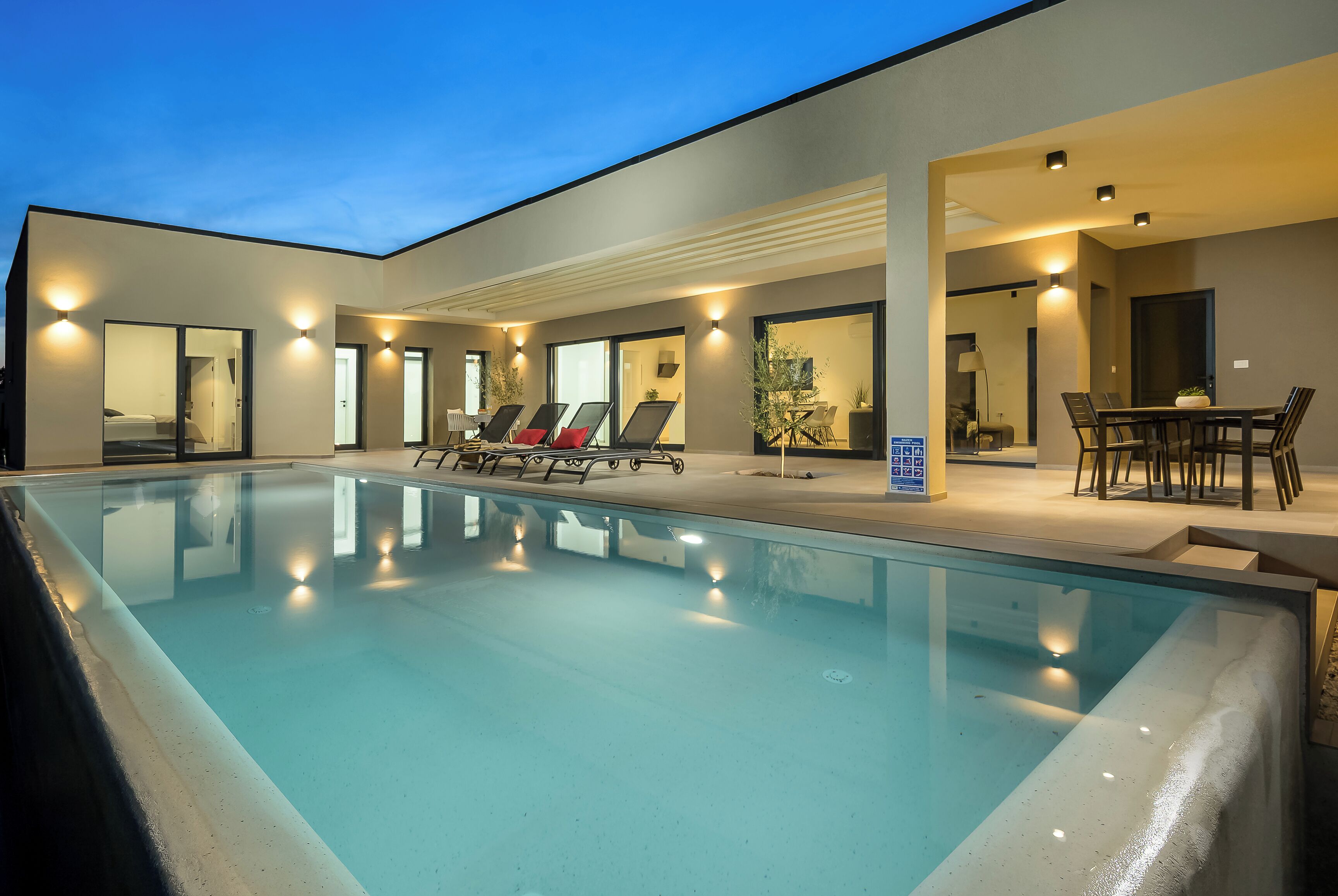 Une piscine intérieure moderne, dotée de chaises longues et d’un espace repas.