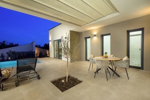 Un patio moderno al aire libre con piscina, zona de estar y un árbol pequeño.