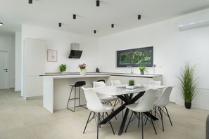 A modern kitchen with a central island, white cabinetry, and a dining area with white chairs. - Villa Yamila (Istria - Žminj) (Žminj)