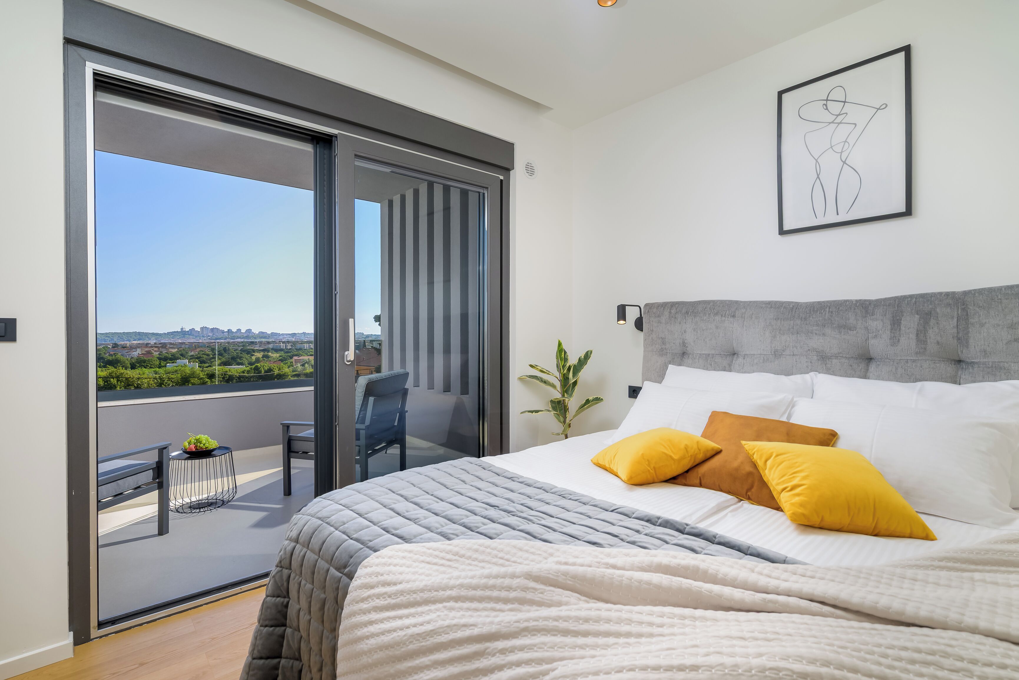 Ein Schlafzimmer mit Bett, einem Balkon und einer Aussicht sowie einem gerahmten Kunstwerk an der Wand.