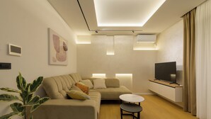 Uma sala de estar moderna com um sofá, uma mesa redonda pequena, uma televisão e uma planta.