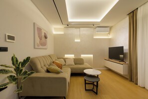 Ein modernes Wohnzimmer mit einer Couch, einem kleinen runden Tisch, einem Fernseher und einer Pflanze.