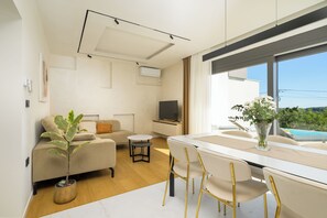 Un salon moderne comprenant un canapé, une table à manger avec des chaises, une petite table ronde, un téléviseur et une plante en pot.