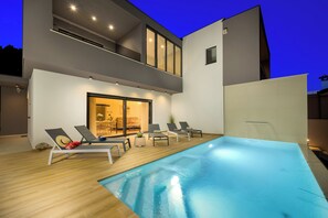 Ein moderner Poolbereich im Freien mit Liegestühlen und Essbereich.