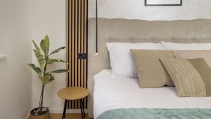 Quarto com cama, almofadas, mesa de cabeceira, planta em vaso e luminária na parede.