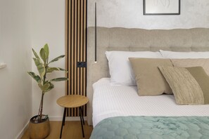 Ein Schlafzimmer mit einem Bett, Kissen, einem Nachttisch, einer Topfpflanze und einer Wandleuchte.