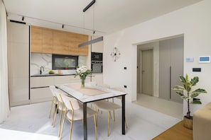 A modern kitchen with a dining area, featuring a marble countertop, wooden cabinets, and a minimalist clock on the wall. - Villa Monte Serpo (Istria - Pula) (Pula)