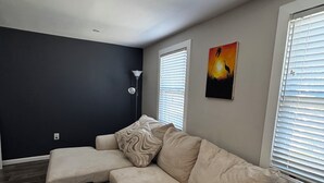 Ein Wohnzimmer mit einer Eckcouch, einem schwarzen Ottomanen und einem Bild an der Wand.