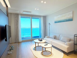 A modern living room with a sofa, two coffee tables, a TV, and a large window with curtains. - Plumbago Yangyang (Yangyang)