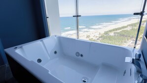 Un baño moderno con una bañera grande, una ventana con vista a la playa y un separador de vidrio.