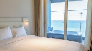 Habitación de hotel con una cama grande, vista al mar y un balcón con jacuzzi.