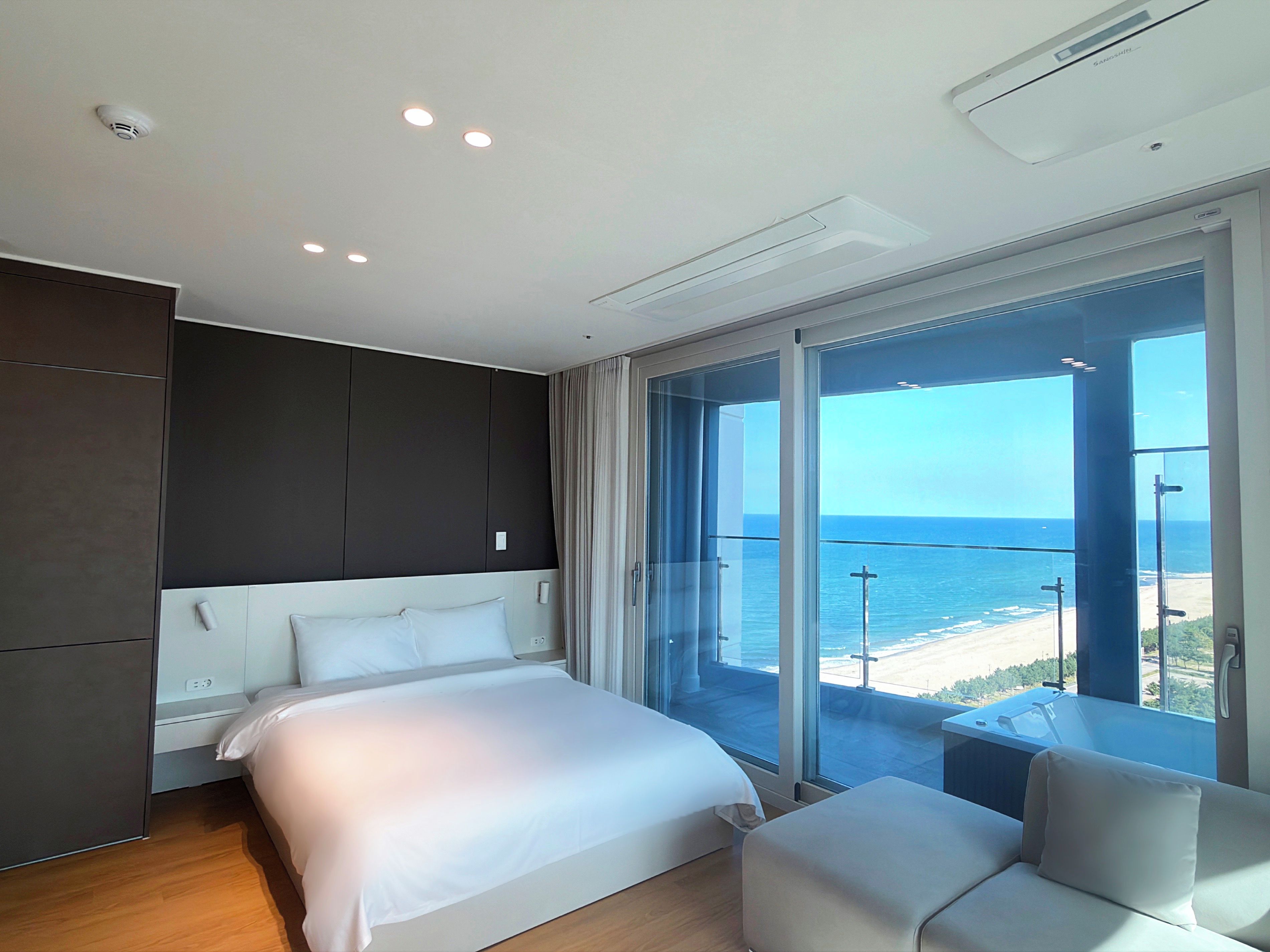 A modern hotel room with a large bed, a seating area, and a balcony with a view of the ocean.