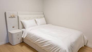 A neatly made bed with a headboard, a bedside table with drawers, and a wall-mounted light fixture.