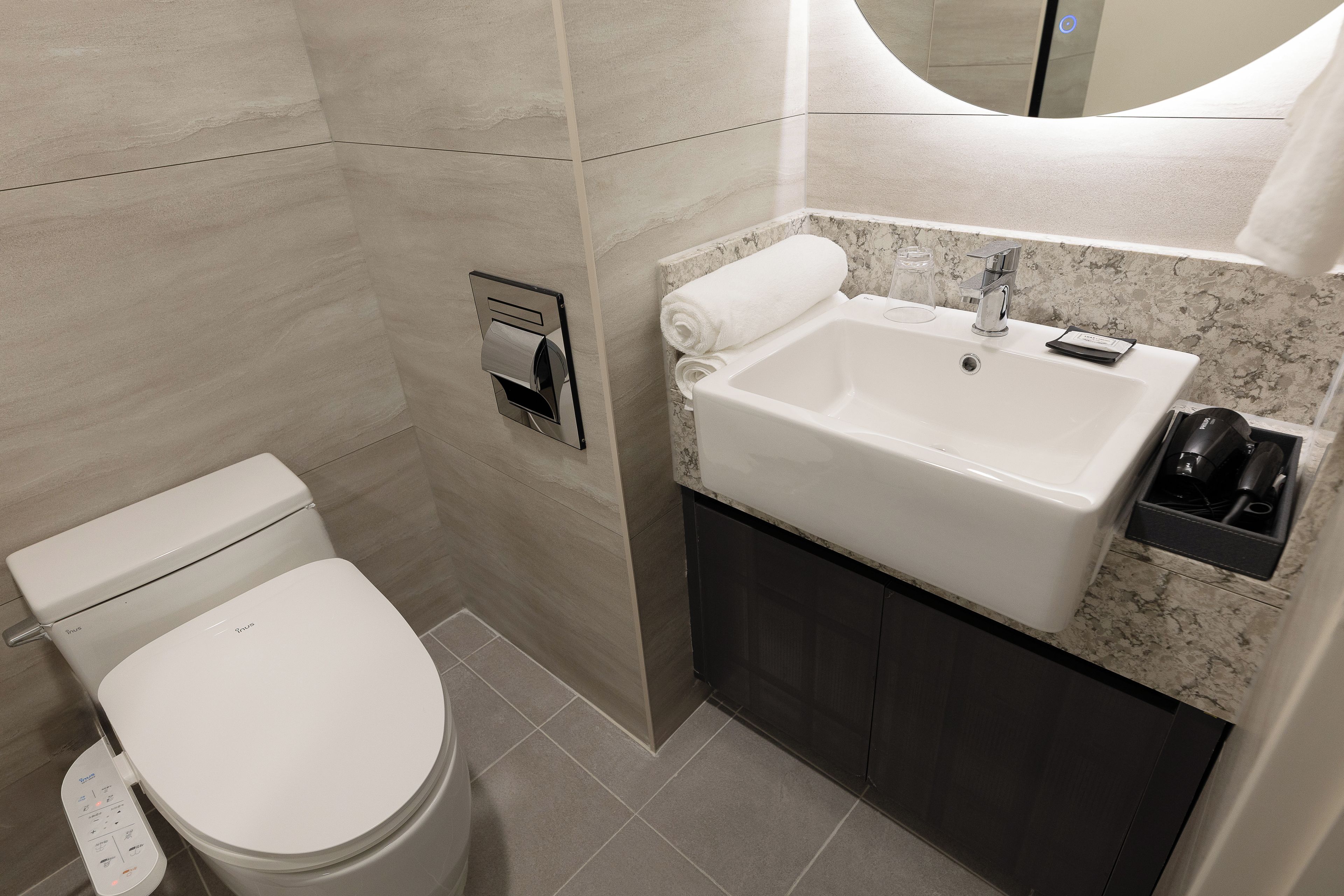 Un baño moderno con inodoro, lavamanos y dispensador de toallas.