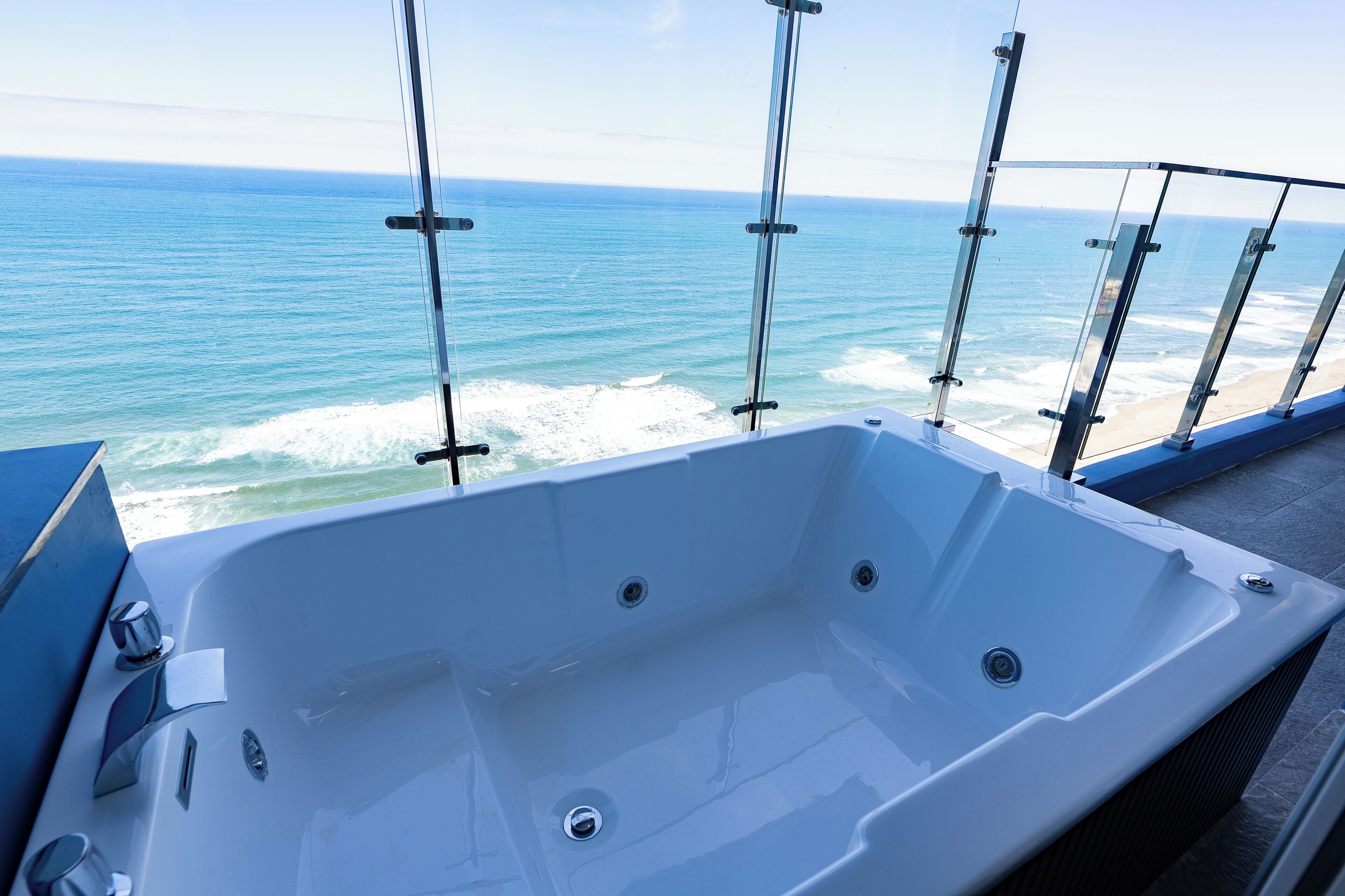 A large, empty bathtub with a view of the ocean through glass railings.