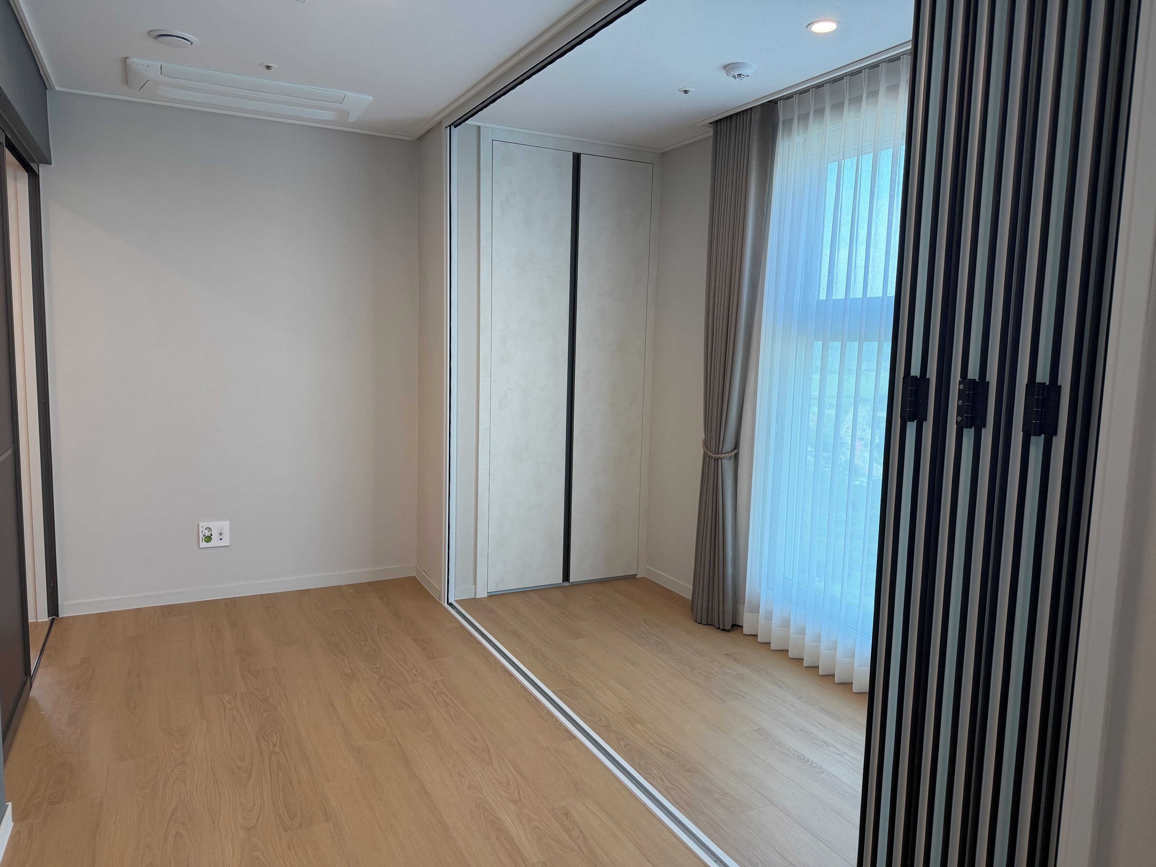 A room with a wooden floor, a sliding door, and a window with curtains.