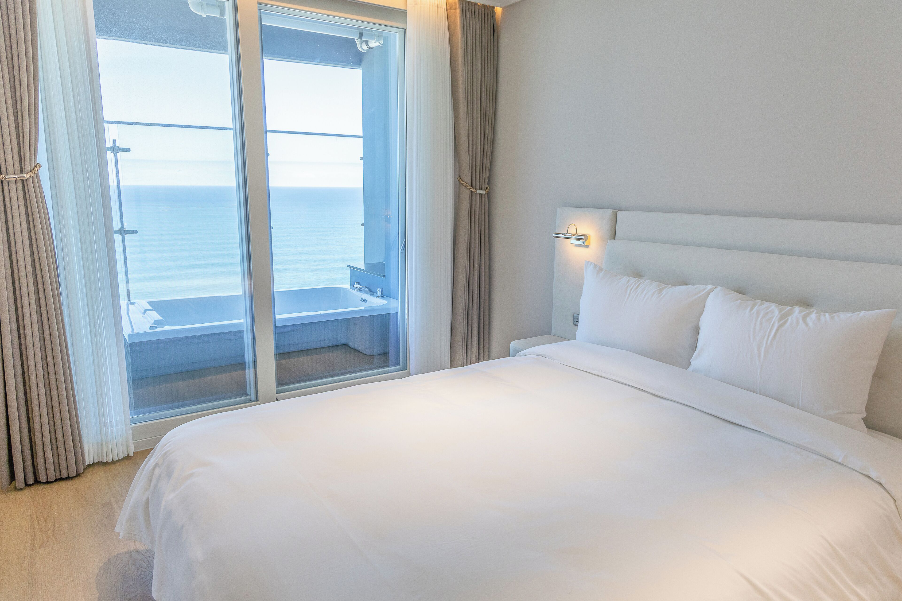Ein Hotelzimmer mit einem Bett, einem Fenster mit Vorhängen und Blick auf das Meer.