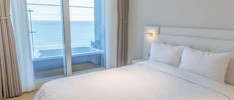 Ein Hotelzimmer mit einem Bett, einem Fenster mit Vorhängen und Blick auf das Meer.