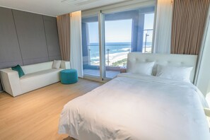 A modern hotel room with a large bed, a sofa, and a view of the beach.