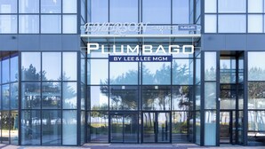 Un edificio moderno con amplios ventanales y un cartel que dice 'PLUMBAGO BY LEE & LEE MGM'.