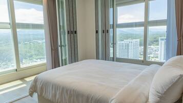 Ein Hotelzimmer mit einem großen Bett, Blick auf eine Stadtlandschaft und einer Schiebetür mit vertikalen Jalousien.