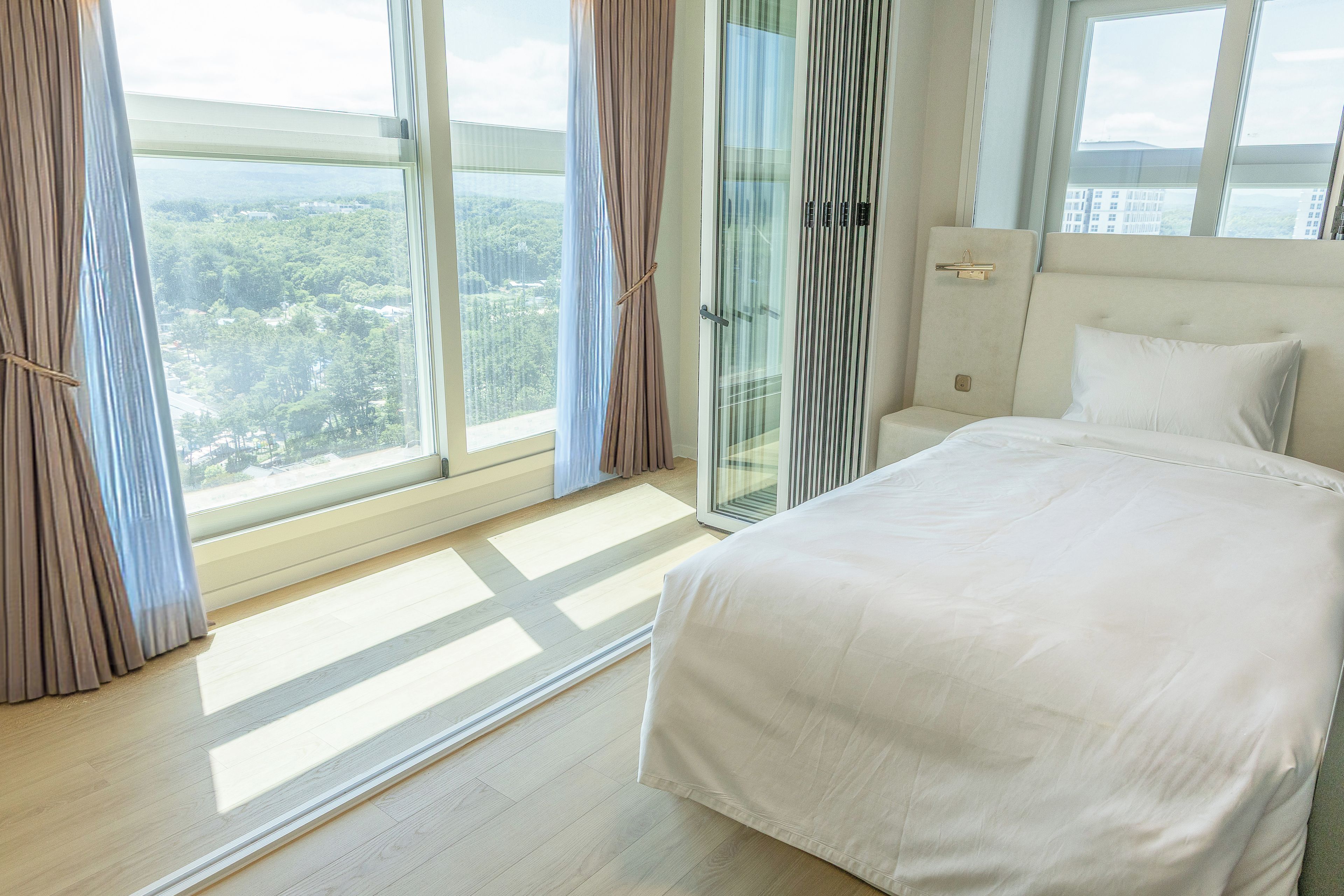 Habitación de hotel con una cama grande, vista a un bosque por la ventana y una puerta corrediza de cristal.
