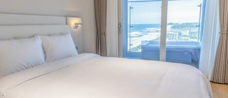 A hotel room with a large bed, a view of the beach, and a cityscape.