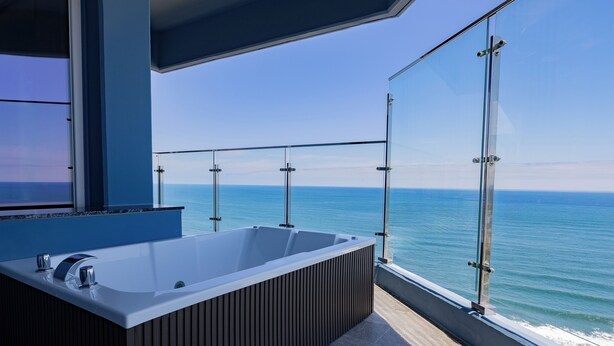 Un baño moderno con una bañera grande, barandillas de vidrio y vistas al océano.