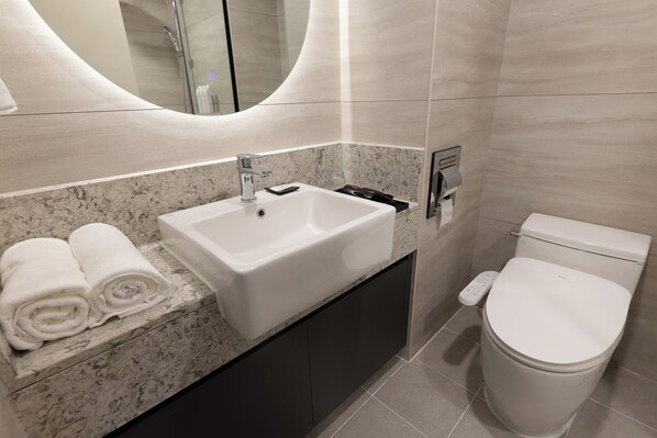 Ein modernes Badezimmer mit Marmorplatte, einem weißen Waschbecken, einer Toilette und einem Handtuchhalter mit gefalteten Handtüchern.