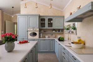 A kitchen with light blue cabinets, a white countertop, and a central island with a vase of flowers and tomatoes. - Vila Da Ella by Istrabook (Krnica)