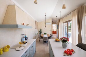 A modern kitchen with a dining area, featuring a central island with a vase of flowers, a coffee machine, and a bowl of fruit. - Vila Da Ella by Istrabook (Krnica)