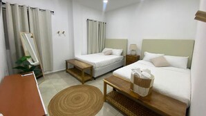 Ein Hotelzimmer mit zwei Betten, einem Schreibtisch, einem Spiegel, einer Pflanze und einem Teppich.