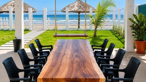 Ein Holztisch mit Stühlen, draußen aufgestellt, mit Blick auf das Meer und den Strand.